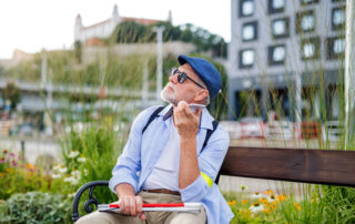 Sight impaired man sitting on a bench listening whilst on his phone