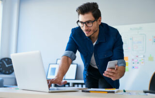 Man looking at his laptop and holding a mobile phone