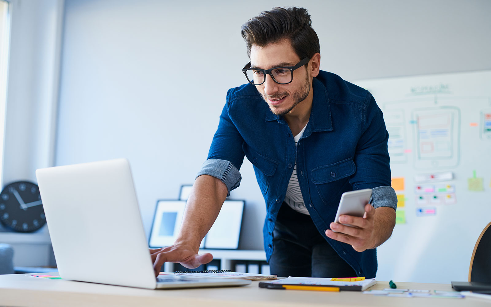 Man looking at his laptop and holding a mobile phone