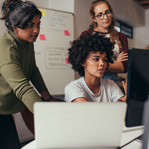 Three women review work on a screen