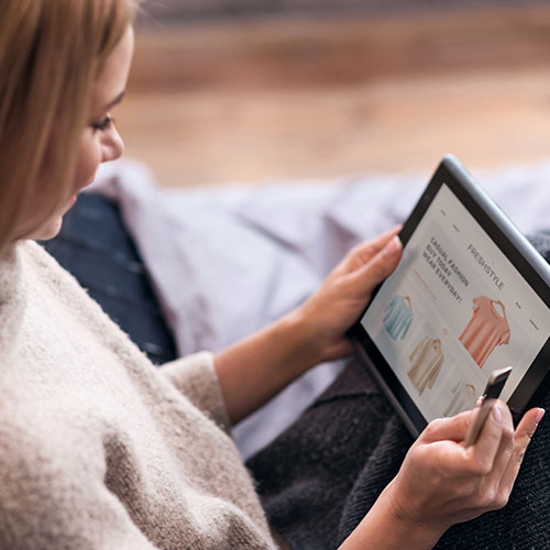 Woman holding credit card and browsing clothing website on her tablet