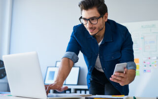 Man holding phone and typing on laptop