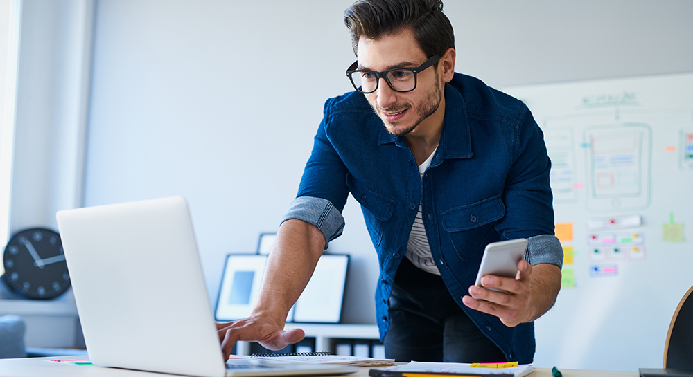 Man holding phone and typing on laptop