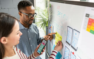 Two people discussing a project with post-it notes and diagrams on a whiteboard