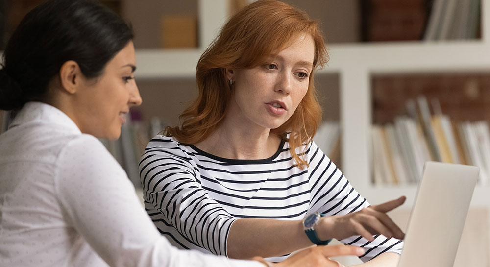 Woman discussing something on laptop screen with colleague